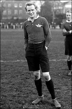 Ronald Poulton Palmer, a white man in rugby kit, standing on a rugby pitch and smiling at the camera. photo courtesy wikimedia commons.